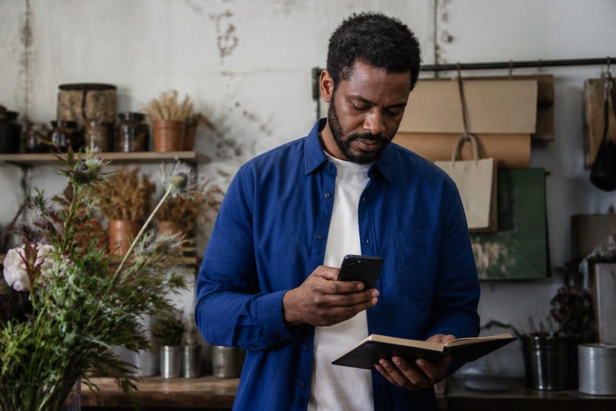 A Black male small business owner checking his phone behind the counter